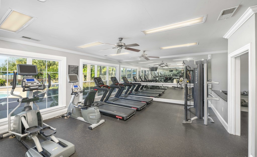 A spacious gym with treadmills, elliptical machines, and a fan.