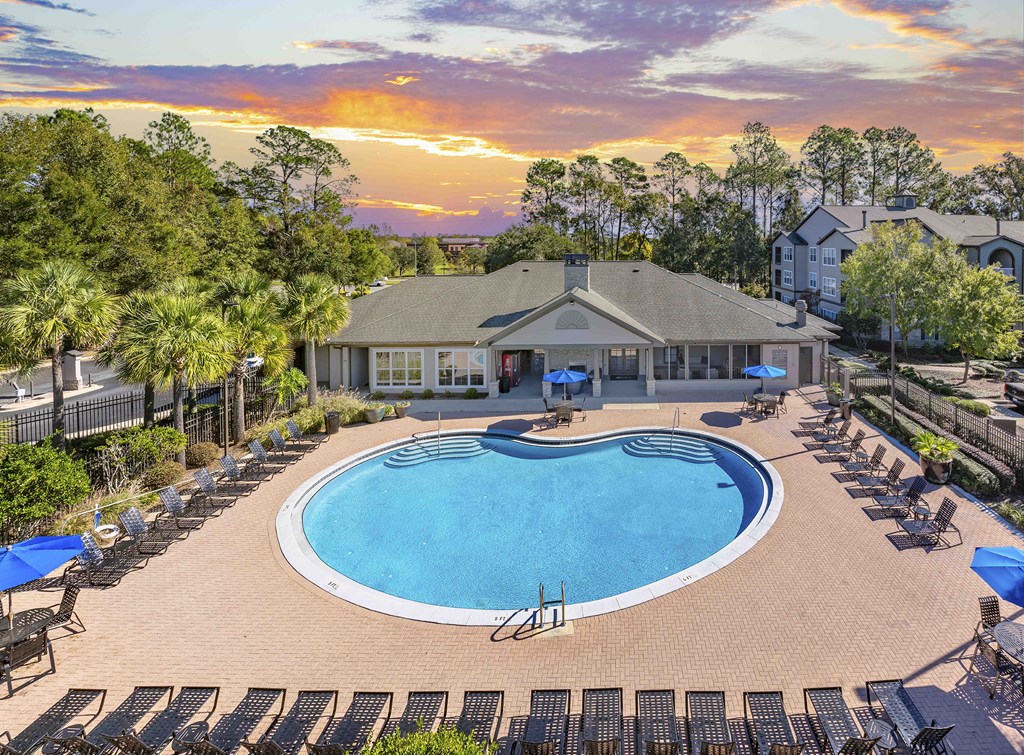 A sunset view of a pool area with lounge chairs and umbrellas.