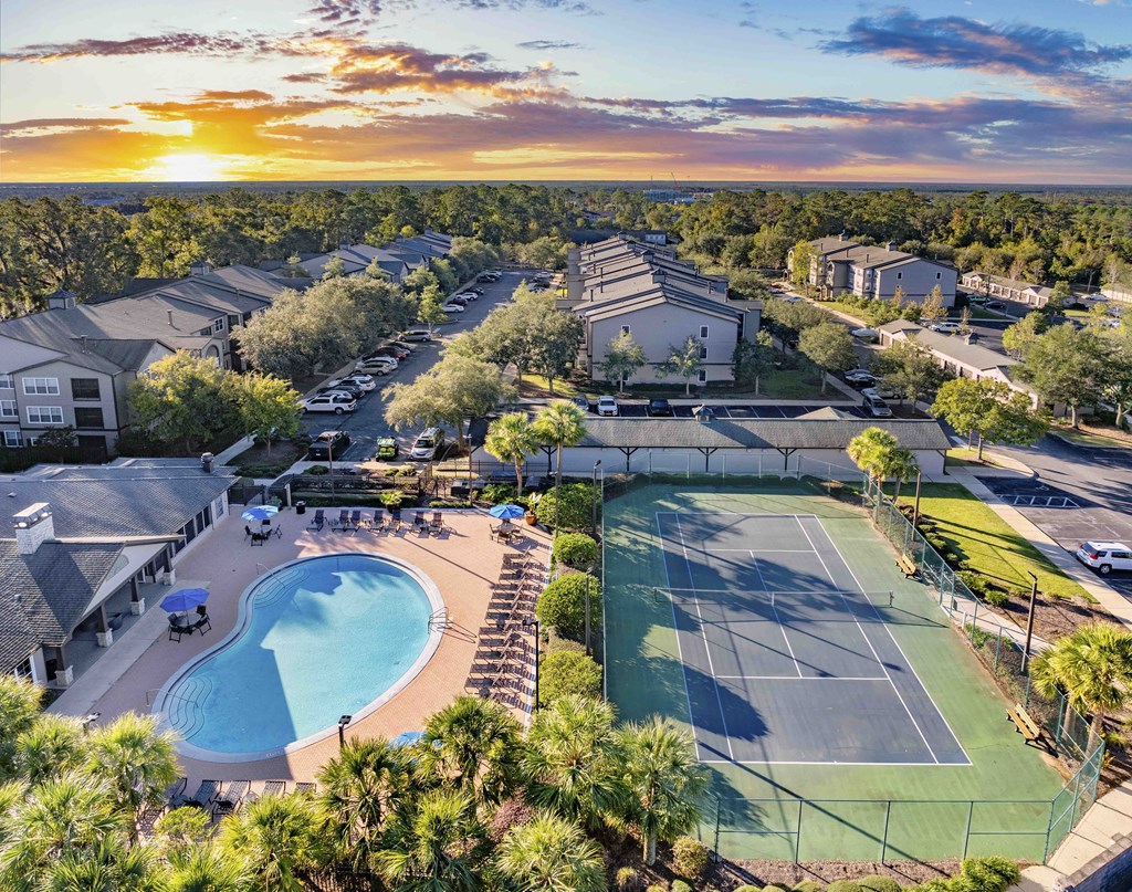 A sunset view of a resort with tennis courts and a swimming pool.