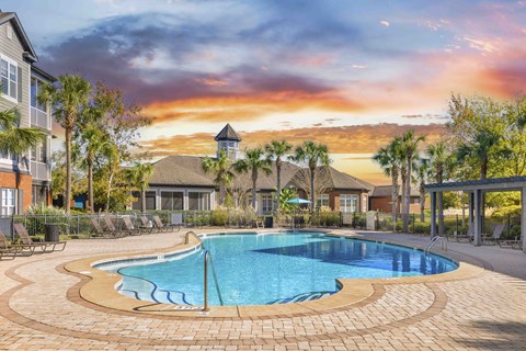 A swimming pool surrounded by a brick patio and lounge chairs.