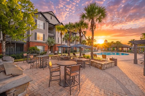 A sunset view of a poolside patio with tables and chairs.