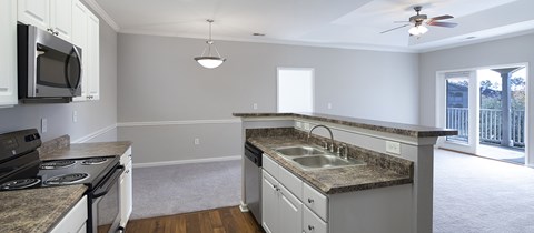 A kitchen with a stove top oven, microwave, sink, and a ceiling fan.