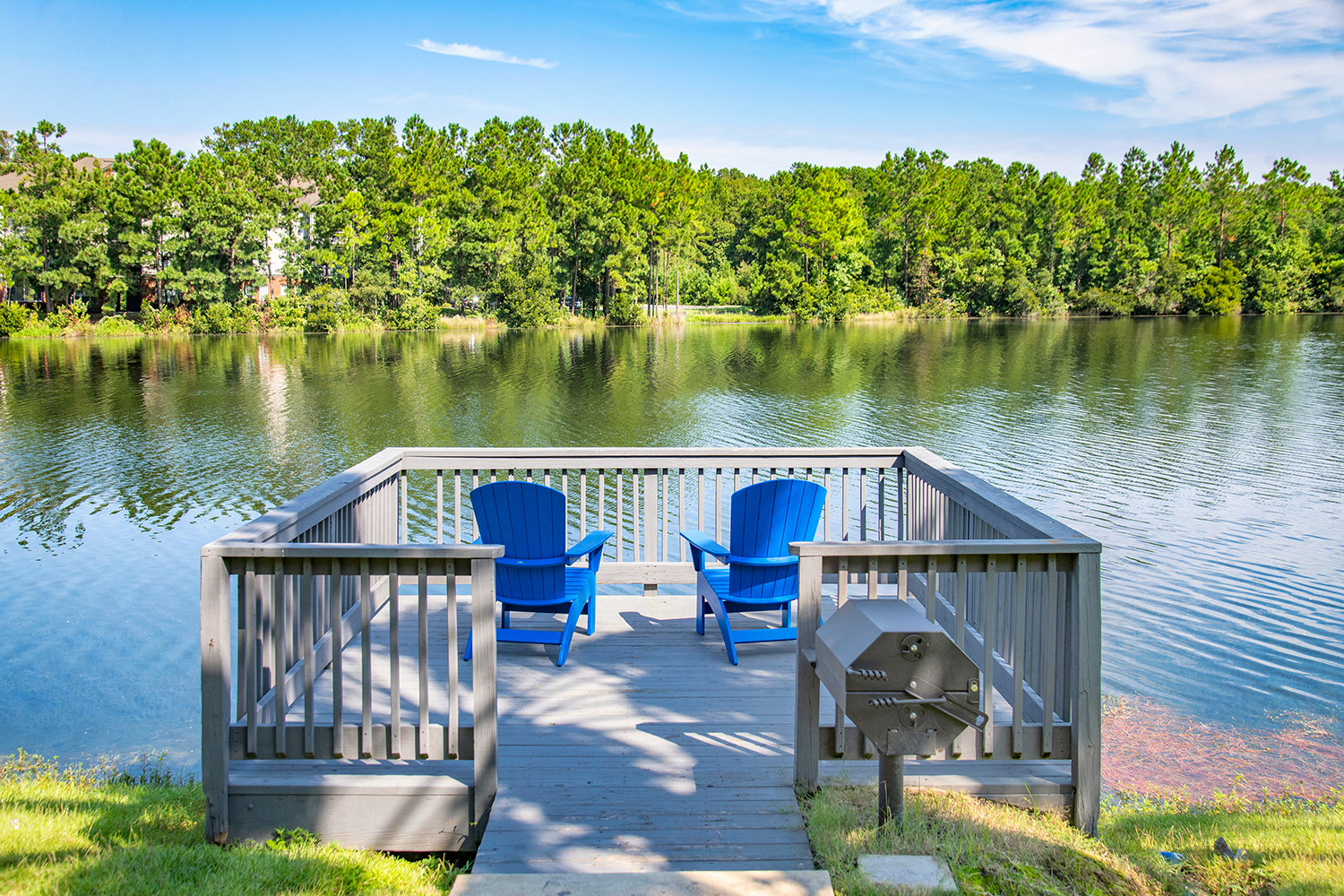 a dock with two blue chairs on the side of a lake
