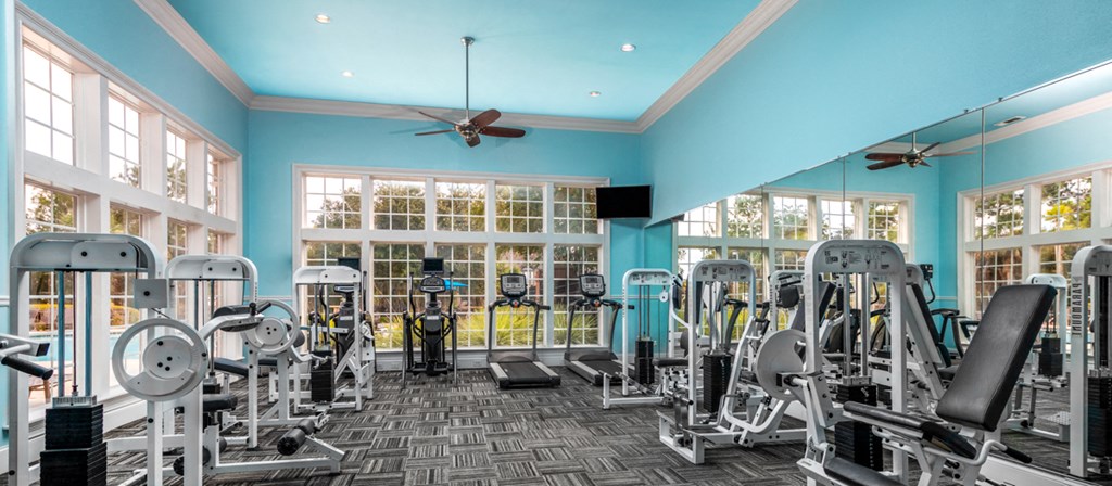 a gym with cardio machines and a ceiling fan