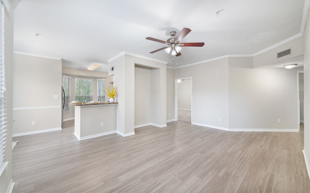 an empty living room with a ceiling fan and a kitchen