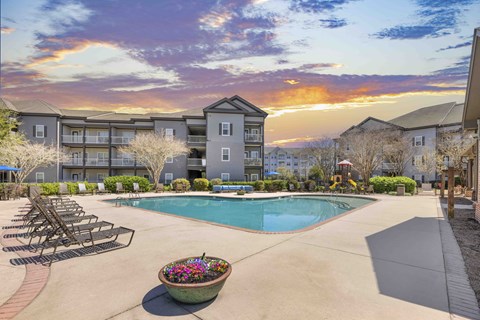 A sunset view of a pool area with lounge chairs and a building in the background.