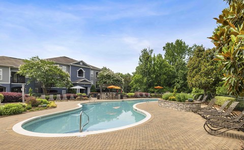 A swimming pool surrounded by a brick patio and lounge chairs.