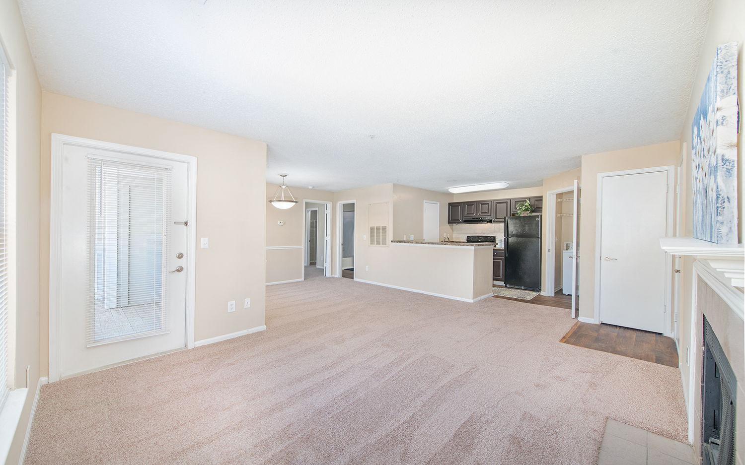 an empty living room and kitchen with a fireplace and a door to the kitchen