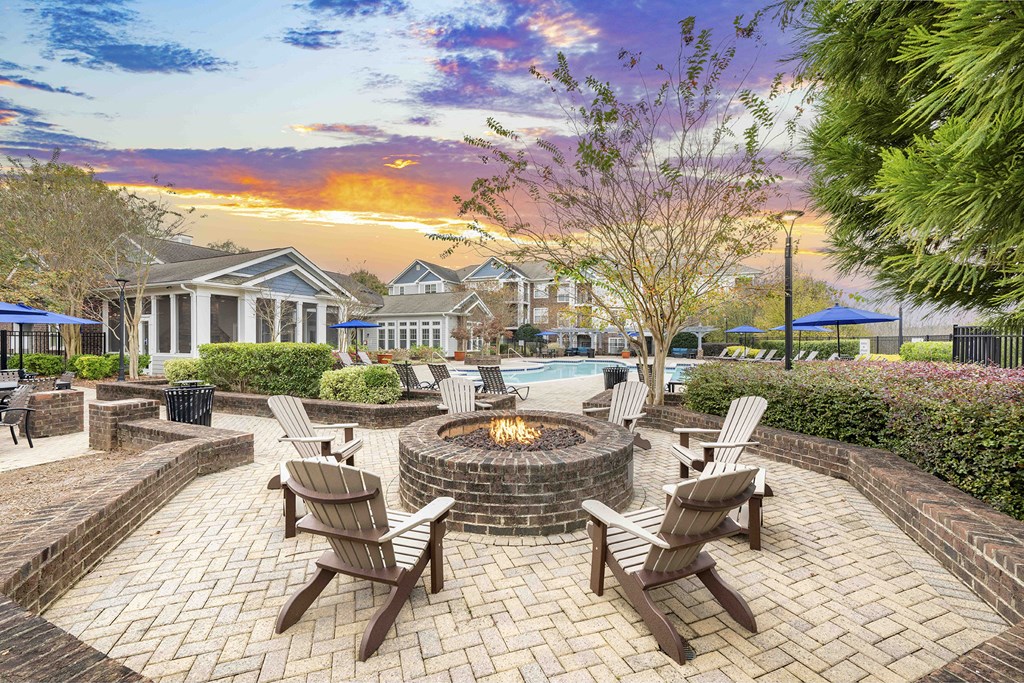 A fire pit sits in the middle of a brick patio surrounded by chairs.