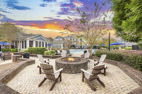 A fire pit sits in the middle of a brick patio surrounded by chairs.