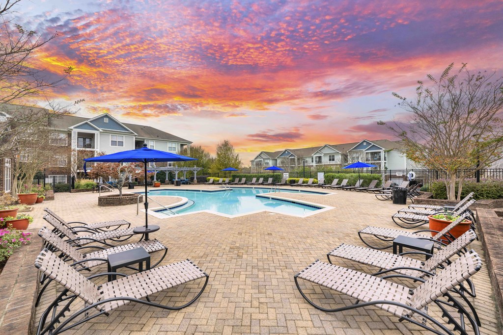 A pool surrounded by chairs and umbrellas with houses in the background.