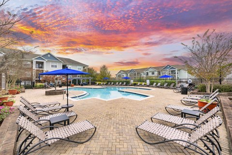 A pool surrounded by chairs and umbrellas with houses in the background.