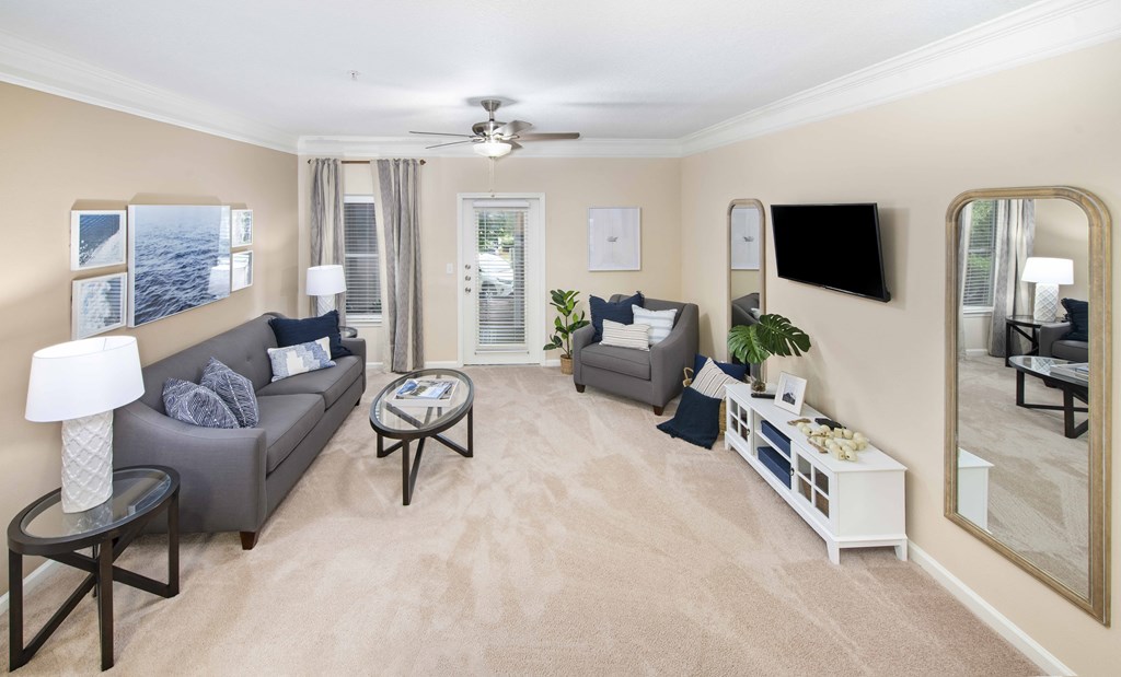A living room with a grey couch, a coffee table, and a flat screen TV mounted on the wall.