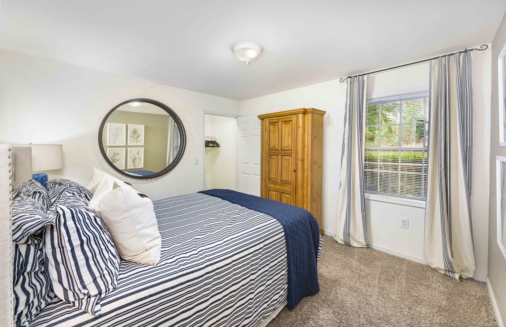 A bedroom with a bed, a mirror, and a window with curtains.