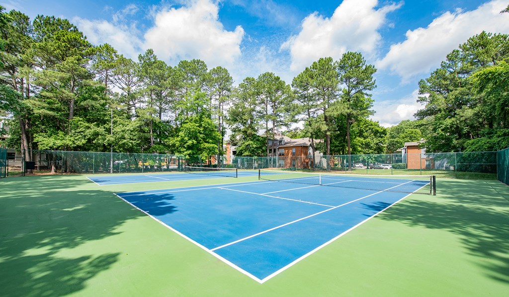 a tennis court with trees and a house in the background