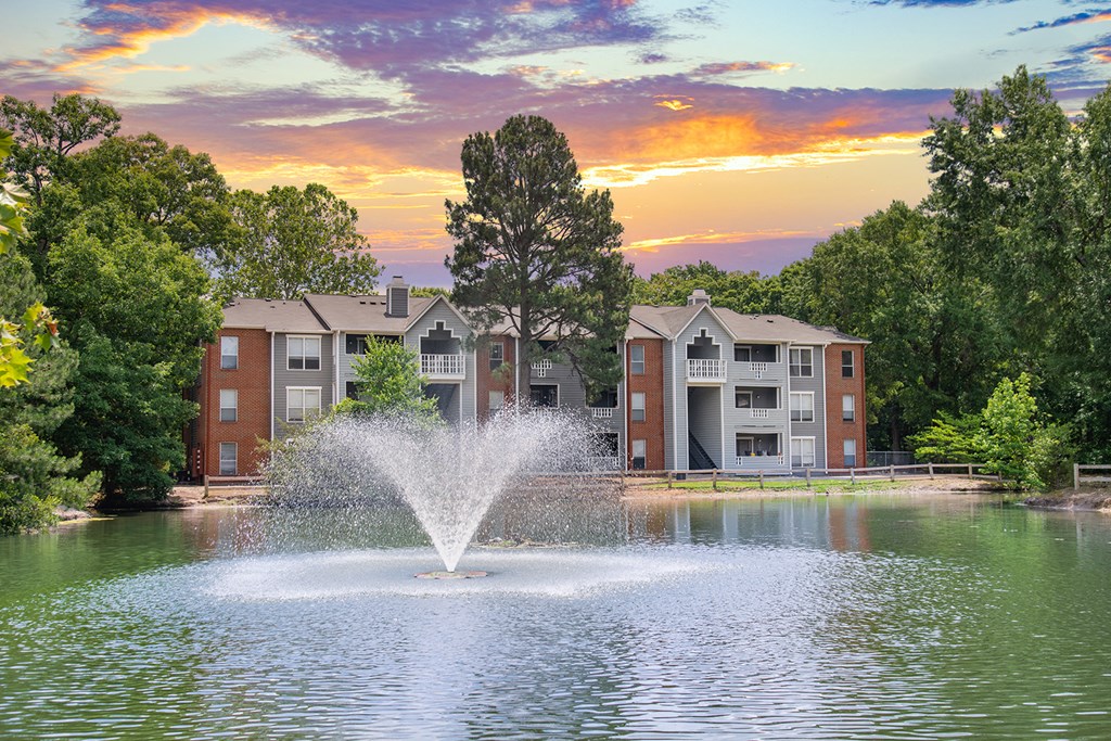 a fountain in a pond with an apartment building in the background