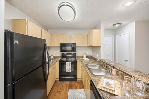 A black refrigerator is in a kitchen with wooden cabinets and a black stove.