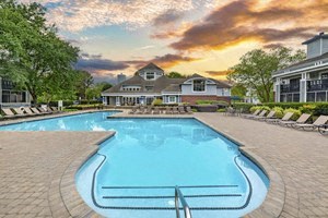 A large swimming pool in front of a house with a sunset in the background.