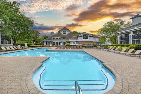 A large swimming pool in front of a house with a sunset in the background.