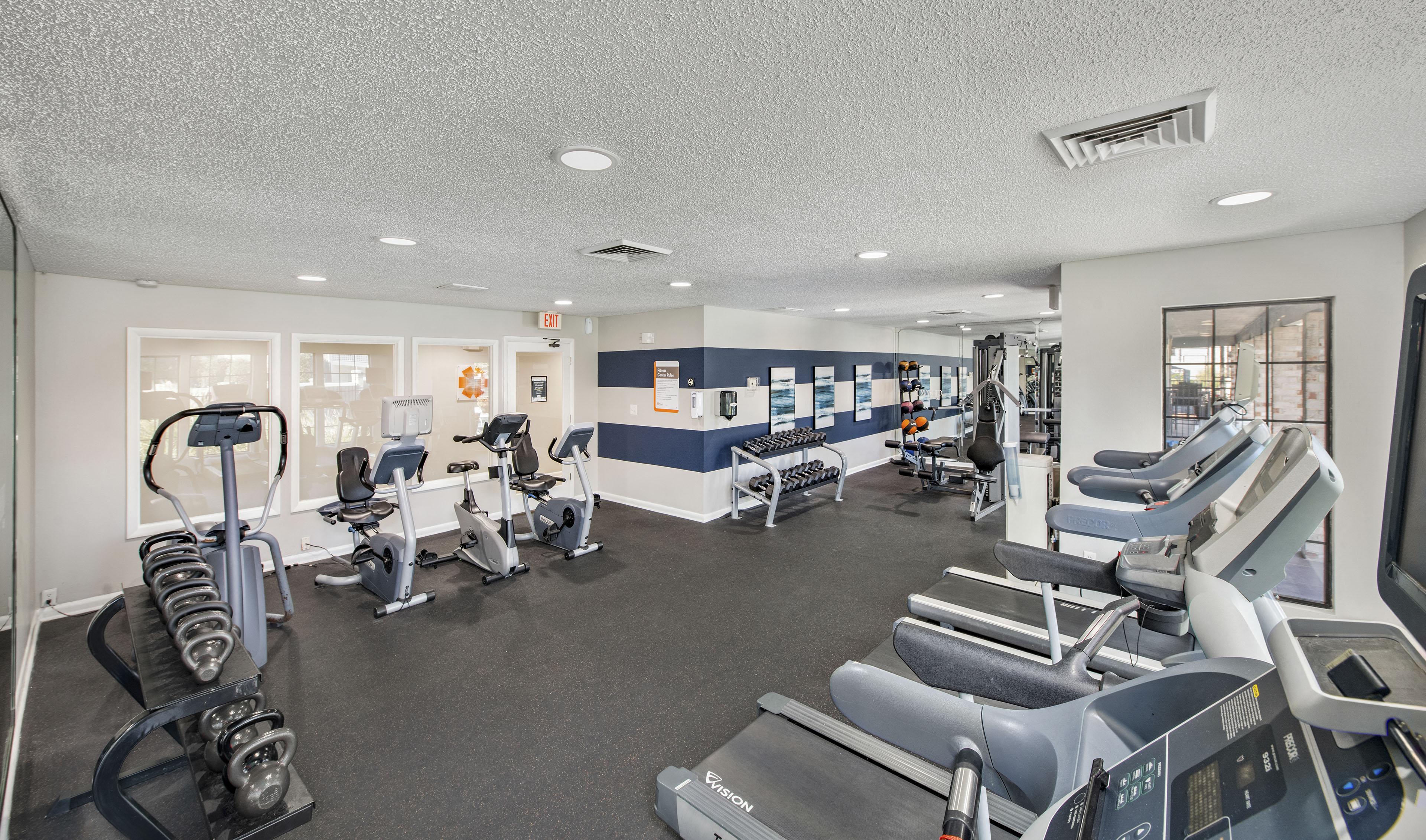 a gym with cardio equipment and weights in a building with windows