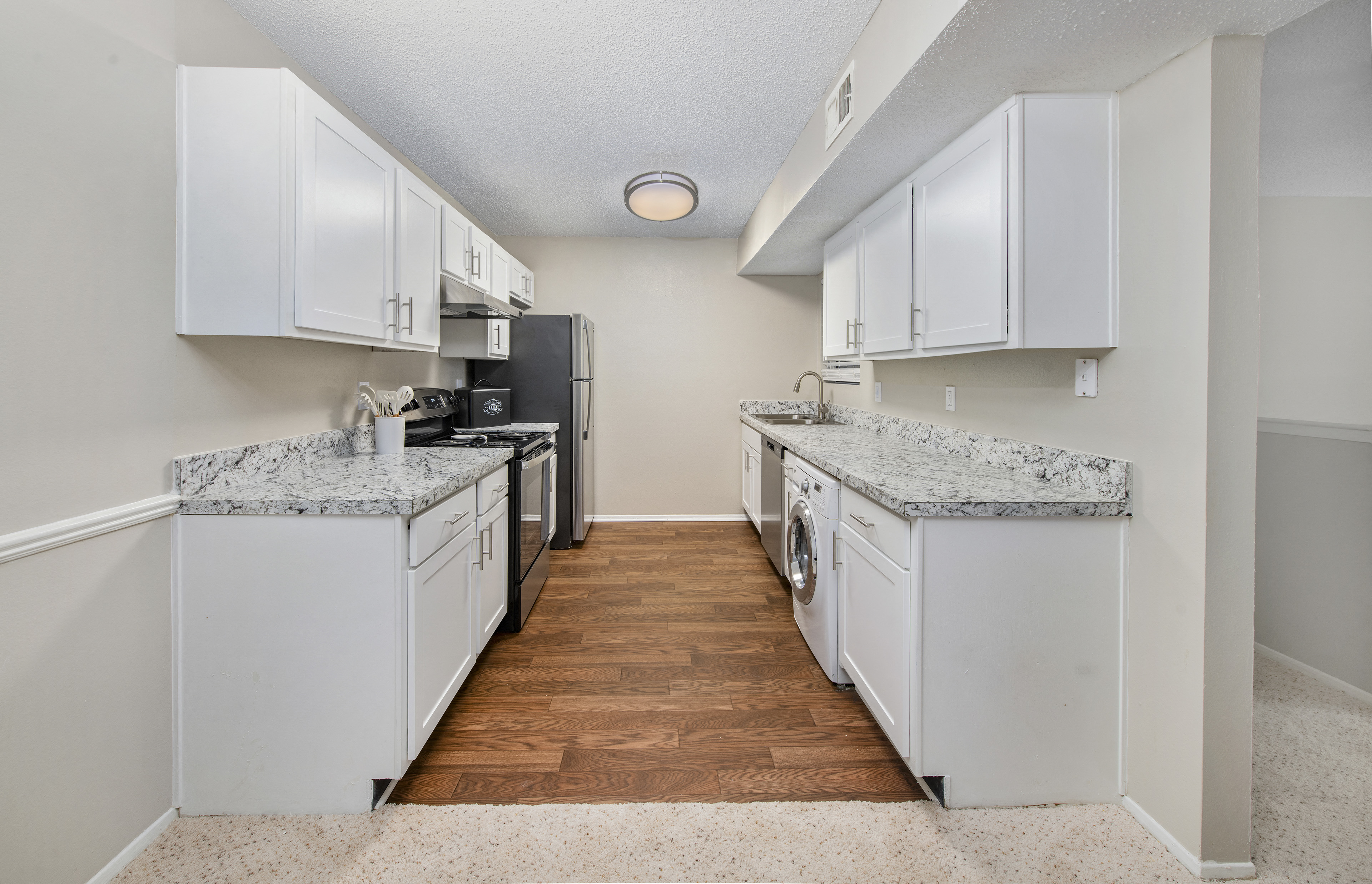 a spacious kitchen with white cabinets and white appliances and wood flooring