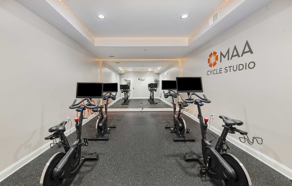 A row of stationary bikes are lined up in a room with the words MAA CYCLE STUDIO on the wall.