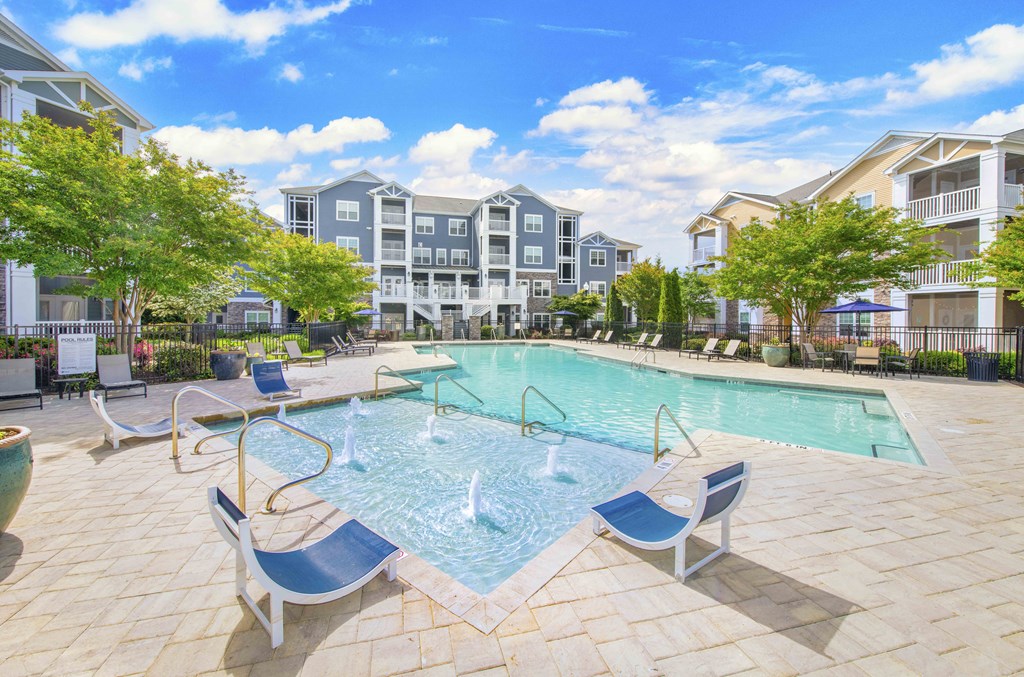 A swimming pool surrounded by chairs and trees in a residential area.