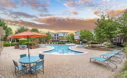 A pool area with a table and chairs and a red umbrella.