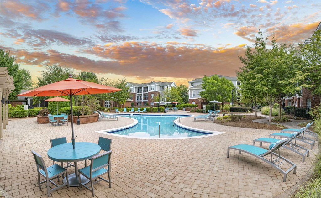 A pool area with a table and chairs and a red umbrella.