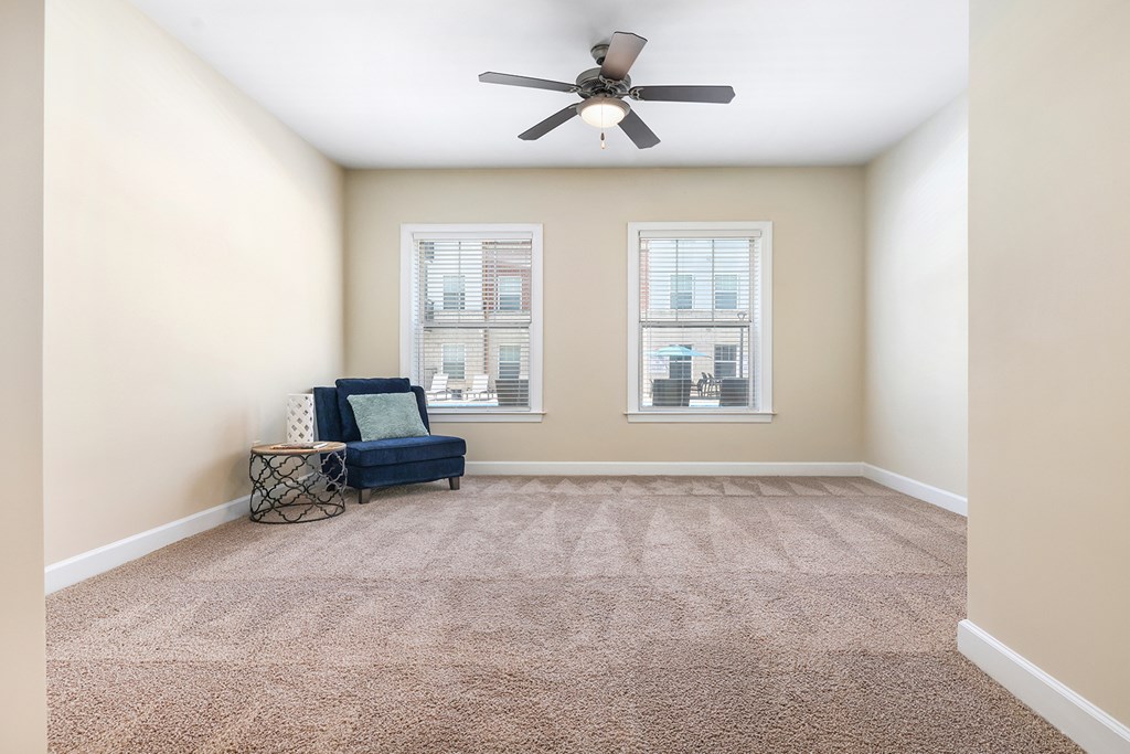 A room with a fan, a sofa, and two windows.