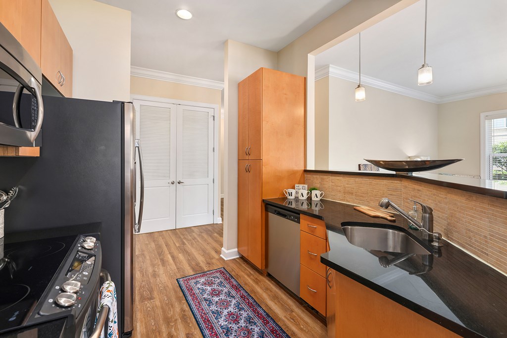 A kitchen with a black refrigerator, wooden cabinets, and a black countertop.
