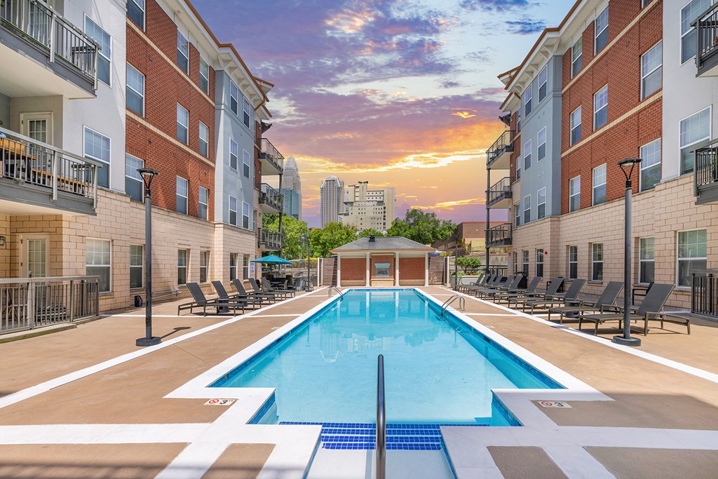 A swimming pool surrounded by lounge chairs and apartment buildings.