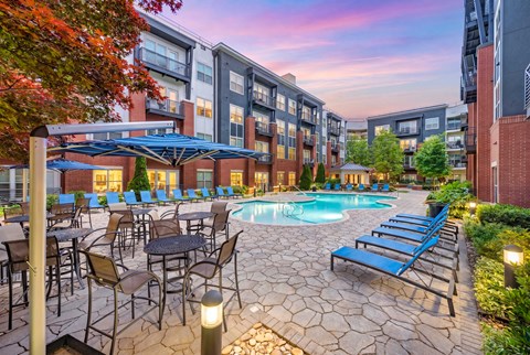 A pool surrounded by chairs and tables is in front of a building.