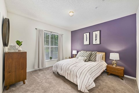 A bedroom with a bed, nightstand, and a plant.