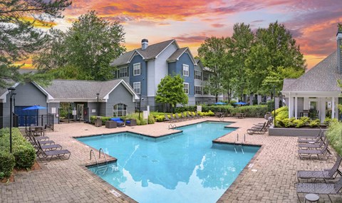 A large swimming pool surrounded by a brick patio and lounge chairs.
