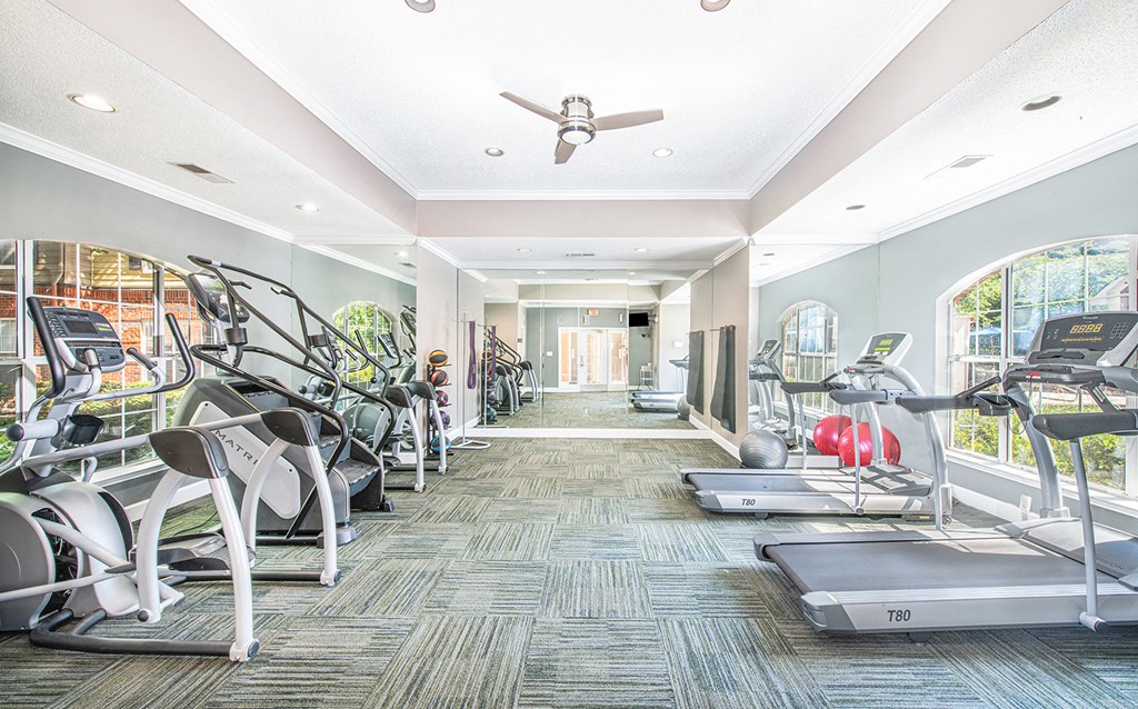 a gym with cardio machines and a ceiling fan
