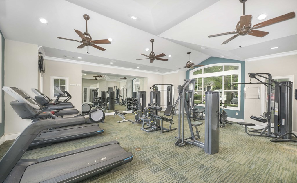A spacious gym with treadmills, exercise machines, and ceiling fans.