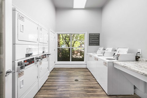 A kitchen with white appliances and a window showing trees outside.