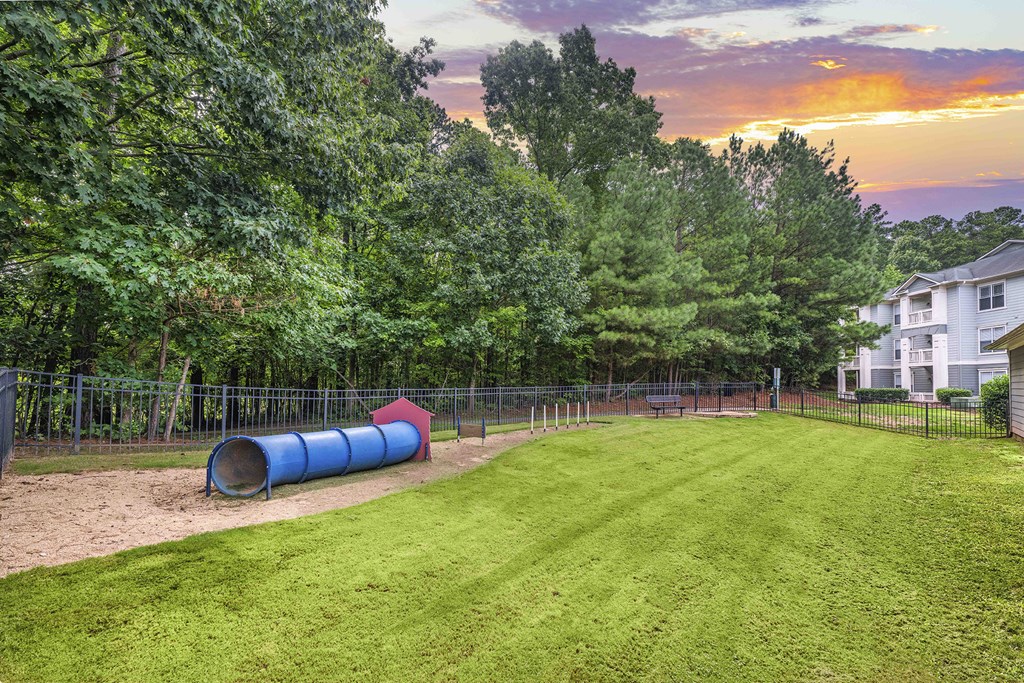 A backyard with a blue barrel and a red object on the grass.