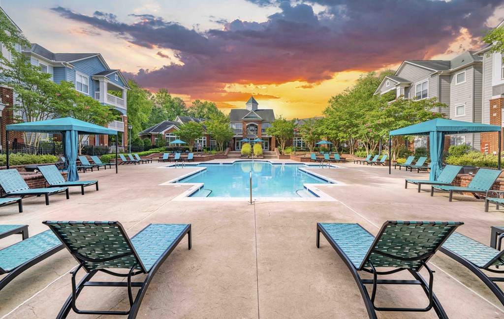 A pool surrounded by lounge chairs and umbrellas at sunset.