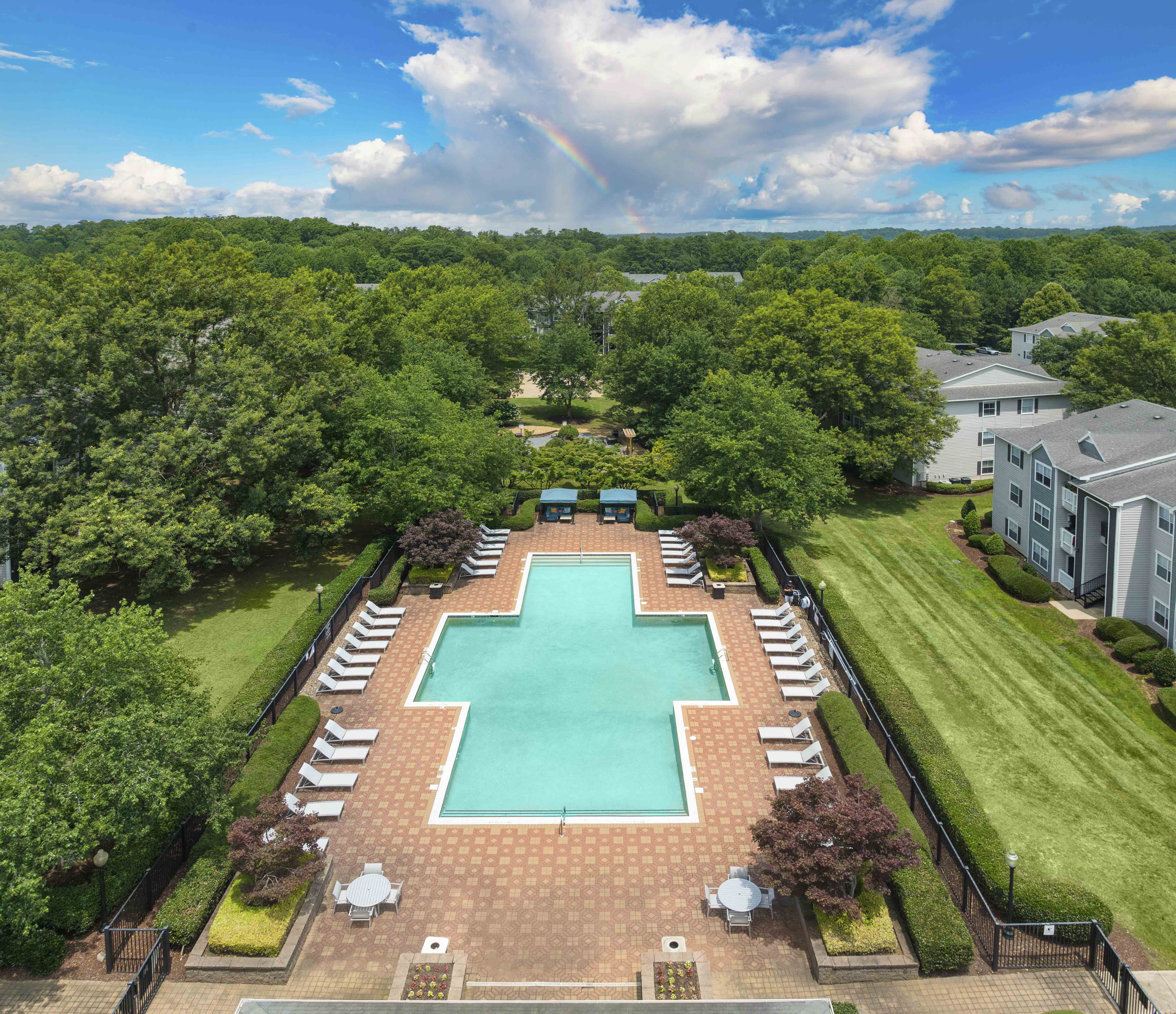 an aerial view of a swimming pool with chairs around it and a yard with trees