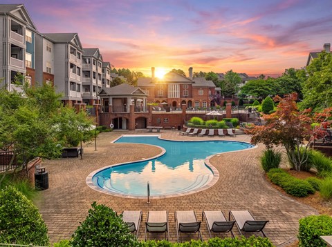 A sunset view of a pool area with lounge chairs and apartment buildings in the background.