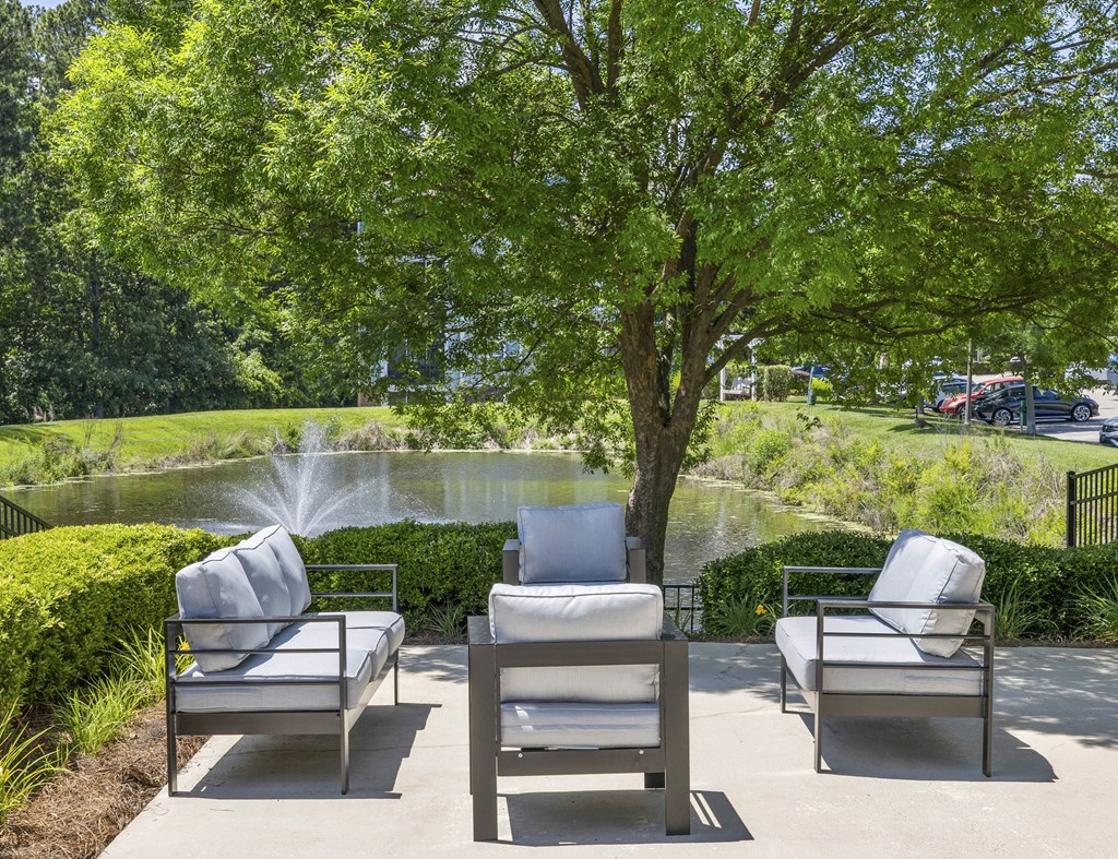 Three white chairs are placed on a concrete surface near a tree.
