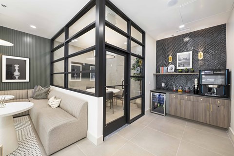 A modern living room with a grey couch and a glass door leading to a kitchen.
