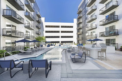 A pool area with lounge chairs and umbrellas in front of apartment buildings.