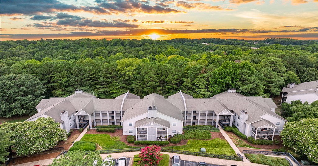 an aerial view of a house with trees and a sunset behind it