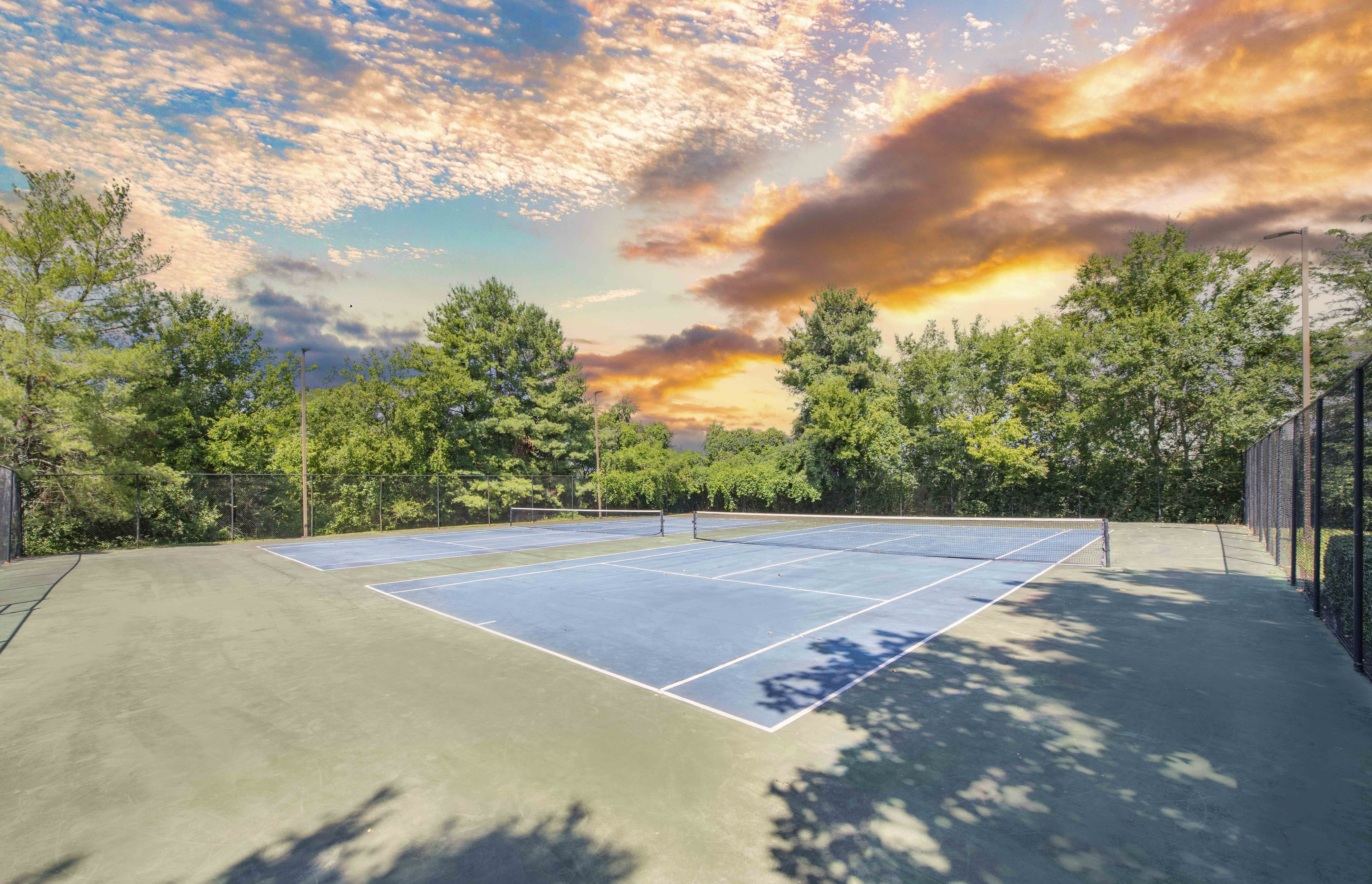 a tennis court with trees and a sunset in the background