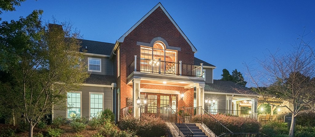 the front of a house at night with a porch and a balcony