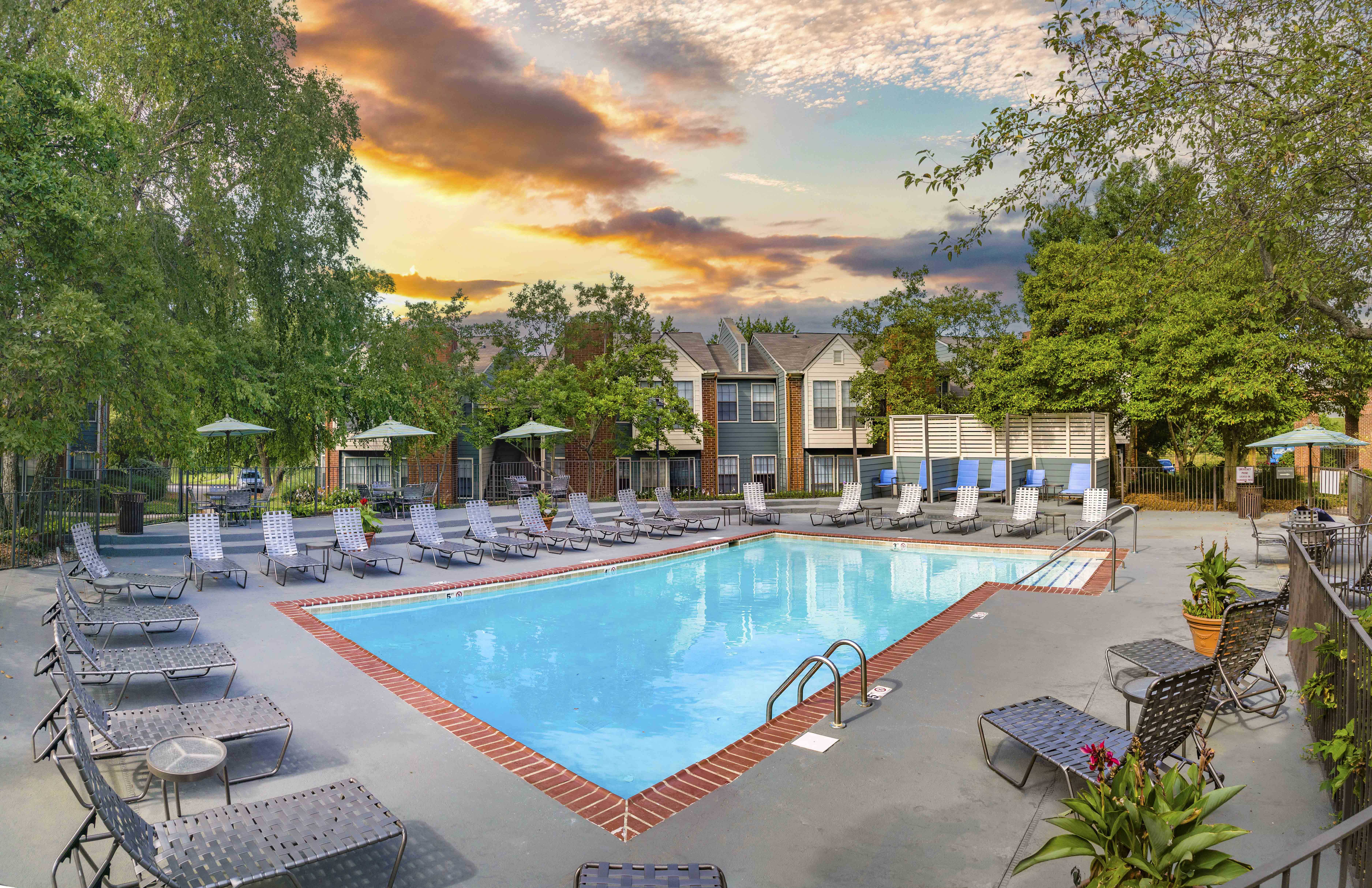 a swimming pool with chairs and umbrellas at sunset