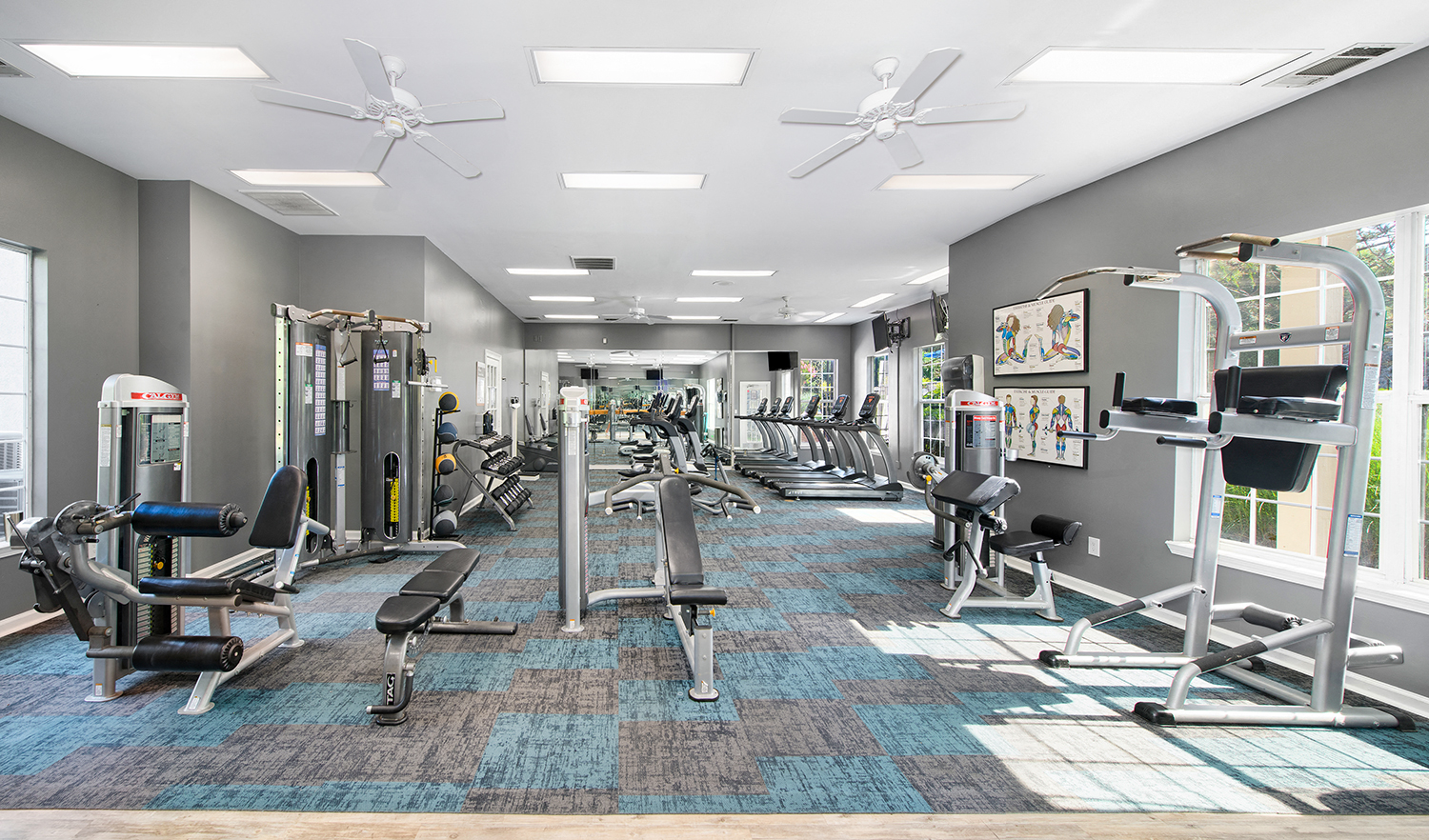 a spacious fitness room with cardio equipment and windows